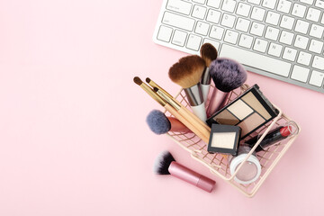 Makeup cosmetic products in shopping cart with keyboard on pastel pink background