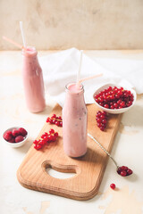 Bottles of tasty smoothie with cranberry and raspberry on light background