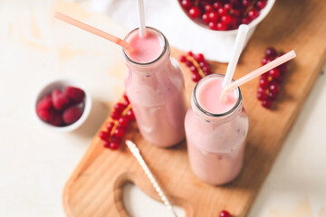 Bottles of tasty smoothie with cranberry and raspberry on light background