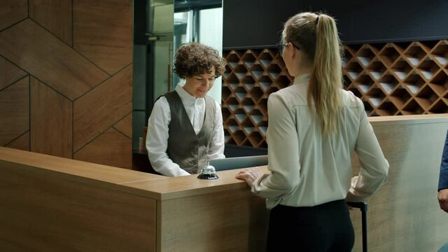 Hotel administrator friendly woman is greeting customers at check-in desk giving key cards talking smiling. Tourism and accommodation concept.
