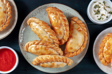 Empanadas, shot from above with various sauces on a dark blue wooden table