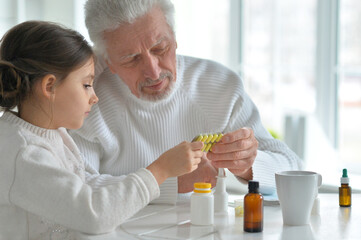 Granddaughter giving medicine to her grandfather in room