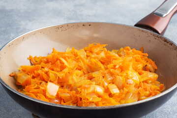 Fry grated carrots and chopped onions with oil in a frying pan. gray concrete background.