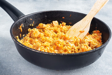 Delicious Asian pilaf, stewed rice with vegetables and chicken in a frying pan. gray concrete background. copy space.