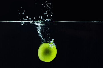 Green apple falling in water with a splash against dark background