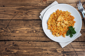 Delicious Asian pilaf, stewed rice with vegetables and chicken on a plate. Wooden rustic background. copy space.