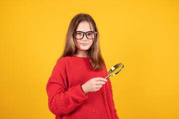 Teen girl holding magnifying glass and looking at something. Young schoolgirl in red sweater and...