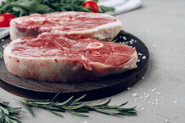Raw rib-eye beef steak on wooden cutting board on gray background