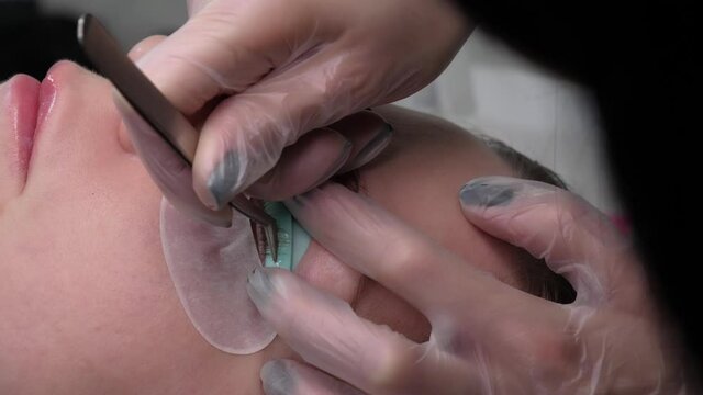 Extension and volumetric extension of long lush eyelashes for a lady in a beauty salon. Young woman with long lush eyelashes undergoes an eyelash care procedure, close-up
