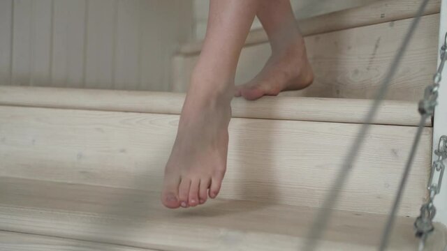 Young woman goes down the wooden stairs barefoot. White steps