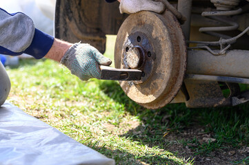 men's gloved hands repair of car drum brake himself. disassembles a jammed disk with a hammer. repair of broken car drum brake disassembled outdoor