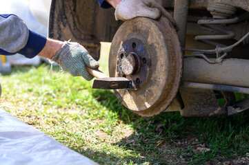 men's gloved hands repair of car drum brake himself. disassembles a jammed disk with a hammer. repair of broken car drum brake disassembled outdoor