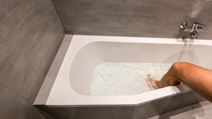 Man going into a bathtub filled with cold water and ice cubes for recovery