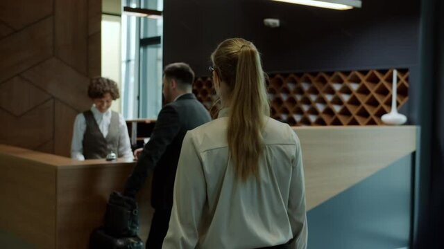 Slow motion of group of guests men and woman checking in hotel talking to friendly reception manager getting key cards. Traveling and lobby concept.