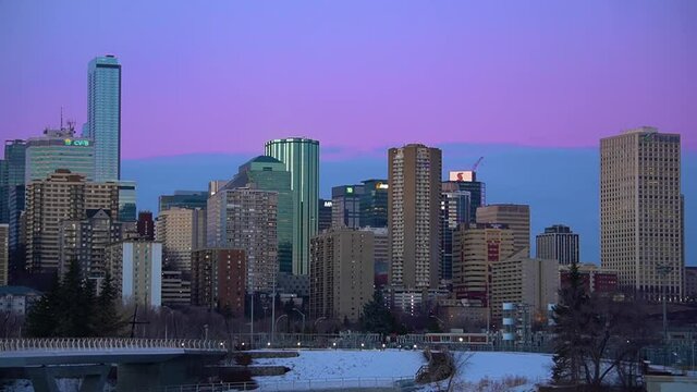4k Looped Purple Blue Sunset Skyline Skyscrappers with winter cyclist pedals bike with backpack on in a black silhuoette crossing the underpass of the Walter Dale modern white bridge with snow ice 1-2