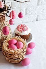 Easter composition with decorated tree branches in a wicker vase, pink colored eggs in wicker basket and Easter cake