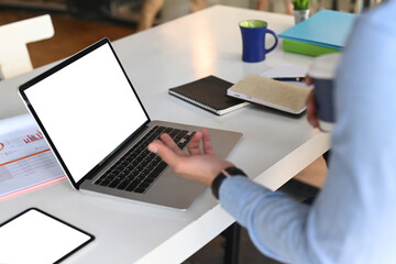 Cropped shot of businessman working with laptop computer and drinking coffee at his office desk.