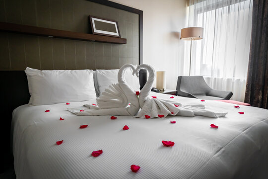 Romantic cosy boutique hotel room getaway with gorgeous swan towels red rose and petals spread on the bed waiting for valentine guests on honeymoon or anniversary