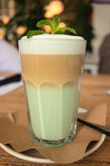 Coffee in the morning. Latte with milk, syrup, whipped cream. Decorated with mint leaves. A glass of coffee on a saucer. Close-up.