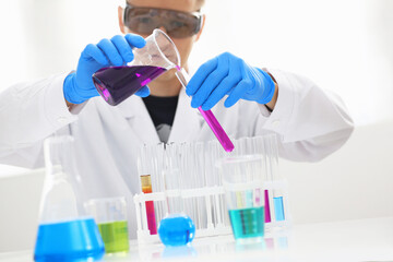 A male chemist holds test tube of glass in his hand overflows a liquid solution of potassium permanganate conducts an analysis reaction takes various versions of reagents using chemical manufacturing