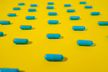 Close up - Blue pills of same color lie on a yellow background. Macro photo. The concept of victory over the coronavirus or vaccination. The end of the pandemic.