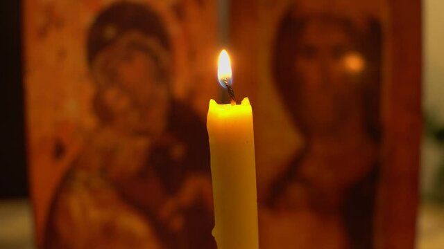 A man's hand lights a church candle with a match against the background of the icon of the Mother of God and Jesus Christ.