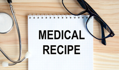 In the notebook is the text of MEDICAL RECIPE, next to the stethoscope and glasses.