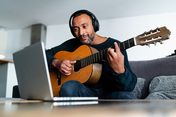 Obraz premium Relaxed man playing the guitar at home and using a laptop