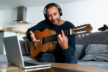 Obraz premium Black man playing the guitar at home and using a laptop