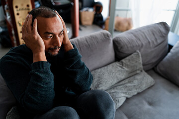 Sad 40 years old man sitting on the sofa at home