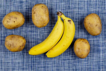 Bananas and raw potatoes on the white and blue table.
