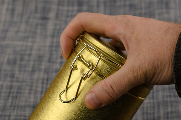A man's hand holding a Tea coffee tin with a clasp close-up.