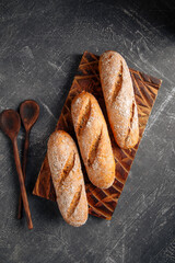 Three loafs of fresh baked baguette on the wooden cutting board on gray background