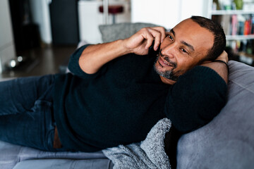 40 years old man relaxing on the sofa at home and talking on the phone