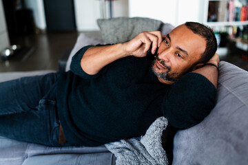 40 years old man relaxing on the sofa at home and talking on the phone