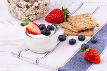 Healthy breakfast with homemade yoghurt and fresh strawberries and blueberries, muesli, crispbread on a white wooden table in rustic style, close up, horizontal