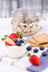 Healthy breakfast with homemade yoghurt and fresh strawberries and blueberries, muesli, crispbread on a white wooden table in rustic style, close up, vertical.