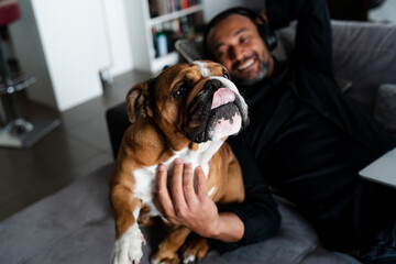 Middle aged man relaxing on the sofa and listening to music next to his dog