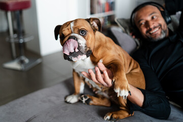 Middle aged man relaxing on the sofa and listening to music next to his dog