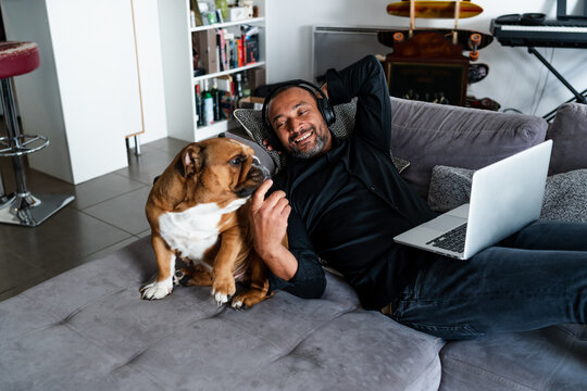 Middle aged man relaxing on the sofa and watching a movie next to his dog