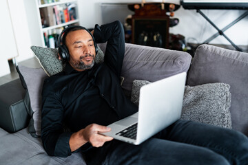 40 years old man relaxing at home using his laptop on the sofa