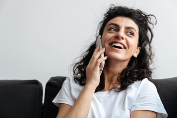 Happy young woman talking on mobile phone while sitting on sofa