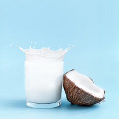 Cracked coconut with splashes of milk in glass on blue background