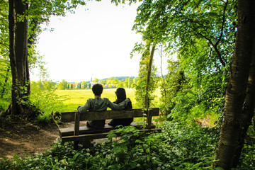 Fototapeta premium distant photo of a couple sitting on a bench together in the middle of the forest.