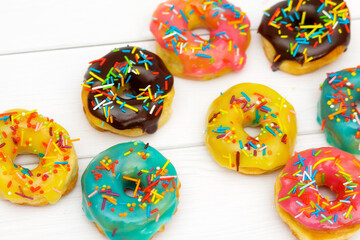Fototapeta na wymiar Homemade donuts with pink, blue, yellow and chocolate glaze with multicolored sugar sprinkles on a white wooden background. Bright background, selective focus