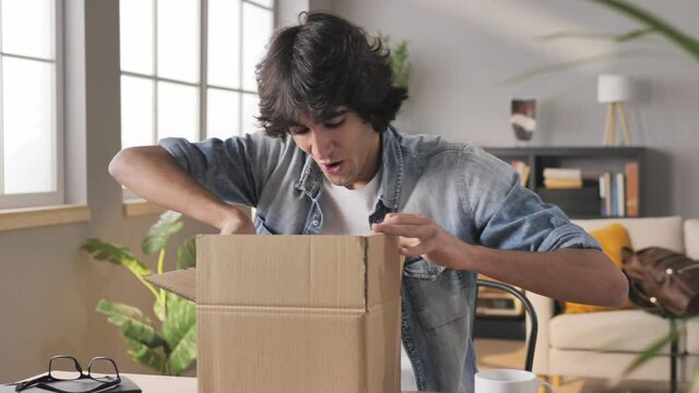 happy young customer man opening a parcel package sitting at his desk,smiling excited consumer male unpacking postal shipping delivery box,satisfied with good purchase