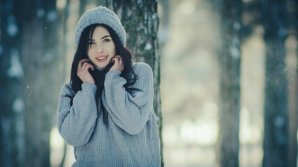 Portrait photo of a young woman among a winter snow-covered forest in a warm sweater and winter hat