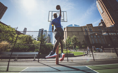 Street basketball athlete performing huge slam dunk on the court, New york buildings background