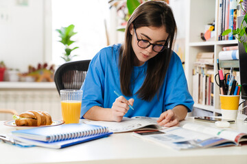 Focused brunette girl doing homework while sitting at table