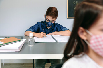 Boy with face mask writing in his notebook at school